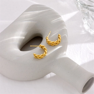 Polished gold-plated twisted rope C-shaped hoop earrings on white ceramic base