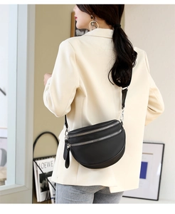 Detail view of black crescent crossbody bag with double silver zippers on a model