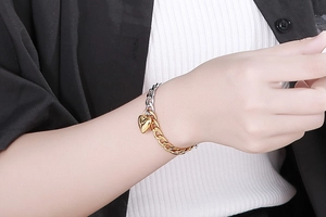 Close-up of dual-tone stainless steel heart pendant bracelet with OT clasp on a wrist