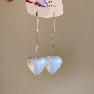 Detail of white pearl heart earrings with golden hooks on a display card held by hand