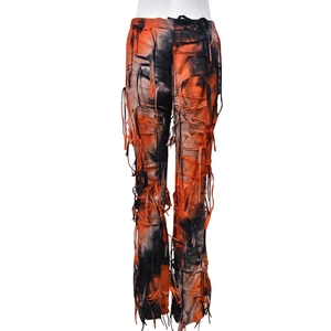 Dettaglio dei pantaloni svasati tie-dye arancioni e neri con texture a frange