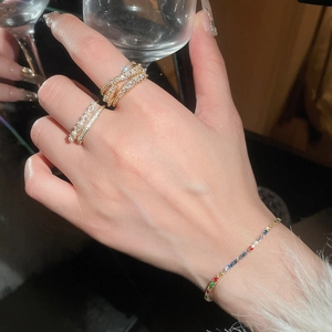 Detail of layered gold zircon rings and a colorful gemstone bracelet worn on hand
