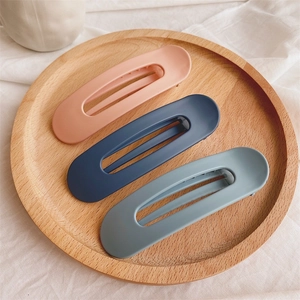 Detailed view of three large matte plastic hair clips in pink, navy, and grey blue colors
