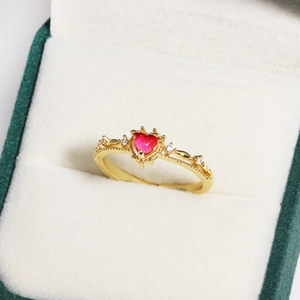 Detail of a gold heart-shaped red gemstone ring with beaded edge and diamond accents