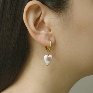 Detail of a golden hoop earring with a heart-shaped porcelain pendant and rose pattern