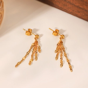 Detail of 18k gold plated stainless steel lip chain fringe earrings on beige surface