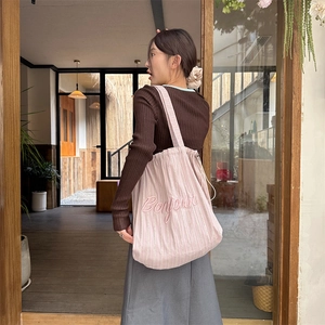Detail of pink corduroy tote bag featuring Bonjour embroidery and white side drawstrings