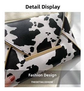 Close-up of black and white cow print envelope clutch with gold metal hardware and stitching