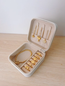 Detailed interior of a cream jewelry box with gold necklaces, rings, and clover charms