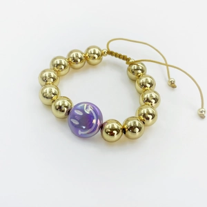 Macro detail of gold beaded adjustable bracelet with purple smiley face charm feature