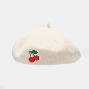 Close-up of embroidered cherry detail on a creamy white wool beret for women