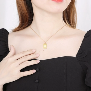 Dettaglio di una collana con ciondolo quadrato dorato con motivo floreale vintage inciso