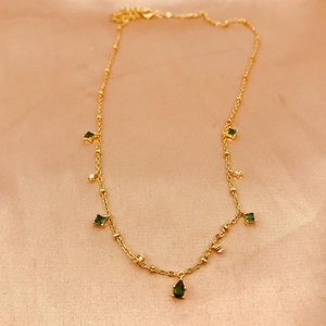 Detail of gold chain necklace featuring green square gemstones and white zircon pendants