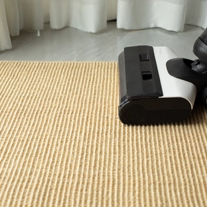 Vacuum cleaner brush cleaning a beige woven natural sisal carpet on tiled floor