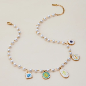 Détail du collier en chaîne dorée avec perles blanches et breloques célestes en émail