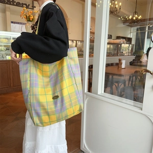 Detail of yellow and purple plaid canvas tote bag with metal logo in a cafe setting