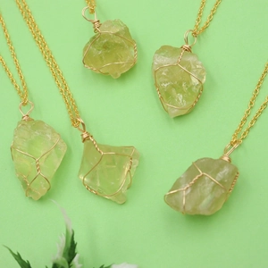 Flat lay detail of natural raw green crystal pendant with golden wire wrap on link chain