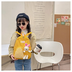Toddler modeling yellow cartoon backpack with plaid pocket and plush bunny accessory