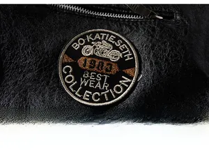 Detailaufnahme von Motorrad-Stickerei und Metallreißverschluss auf schwarzer Kunstlederjacke