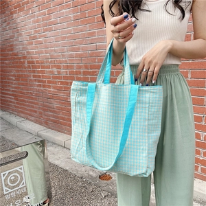 Detalle del bolso tote de lona a cuadros azules con asas reforzadas sobre ladrillos