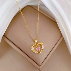 Detailed close-up of gold heart necklace with pink gemstone and crystal bow on silk