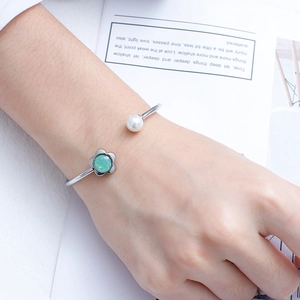 Detail of silver open bangle featuring green flower crystal and white pearl on wrist