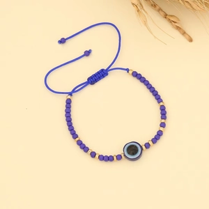 Detail of adjustable blue bead bracelet featuring evil eye charm and woven pull string