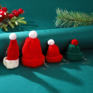 Close-up of festive knitted Christmas hat earrings with pom-poms on a green pine background