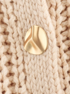 Close-up of irregular gold metal button on beige chunky knit cardigan texture