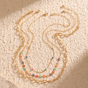 Detail of layered gold necklaces with colorful enamel flower charms and vibrant beads