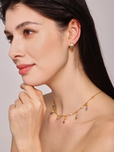 Close-up of model wearing gold earrings and necklace with colorful square-cut gemstones