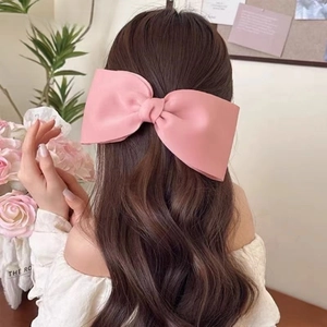 Pink oversized matte satin bow hair clip styled on long wavy hair in an elegant updo