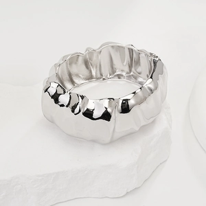 Detailed close-up of a silver irregular textured wide cuff bangle on a stone pedestal