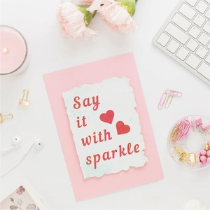 Close-up of glitter letter sticker saying Say it with sparkle on card with pink carnations