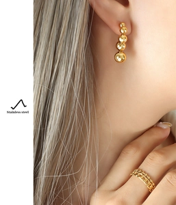 Detail of gold-plated stainless steel ball drop earrings and double-layer ring on model