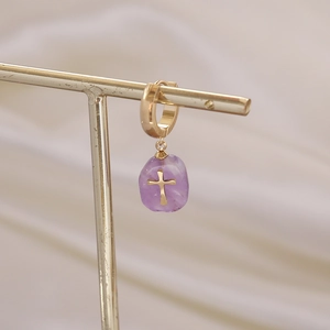 Vue détaillée d'une croix dorée sur une boucle d'oreille avec pierre violette
