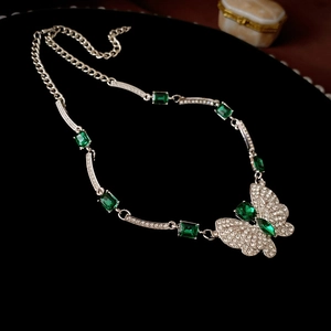 Detailed view of silver butterfly necklace with emerald green crystals on black velvet
