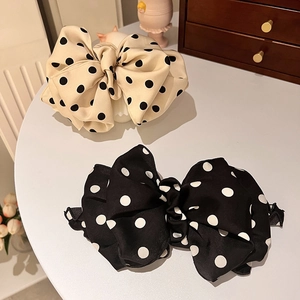Polka dot bow hair clips in black and cream satin on a white table in a cozy home setting