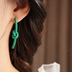 Detail of green knot-shaped matte earrings worn on a model with professional lighting