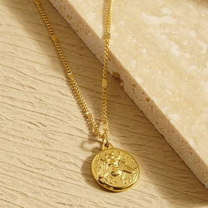 Minimalist gold necklace with a honeybee embossed pendant on a neutral stone background