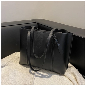 Large black leather tote bag on white knit blanket with a modern minimalist texture