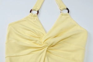 Detail of yellow halter neck dress featuring a twisted bodice and tortoise ring hardware