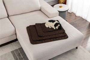 Quilted coffee-colored pet mats in four sizes stacked on a modern grey fabric sofa