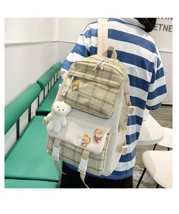 Detail of cute beige plaid canvas backpack featuring teddy bear pendant and fashion badges