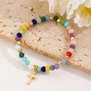Detailed shot of colorful beaded bracelet with gold cross charm on natural stone