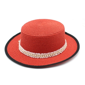 Detail of red boater straw hat featuring faux pearl and white lace ribbon decoration