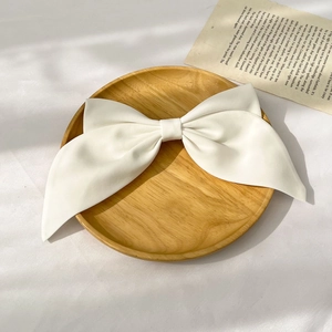 Top view of a white satin bow hair clip on a wooden tray with soft lighting and shadow