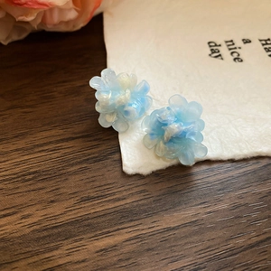 Macro shot of 3D ice blue and pearlescent flower earrings on a textured wooden background