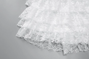 Detail of white lace jumpsuit featuring layered ruffles and delicate floral embroidery