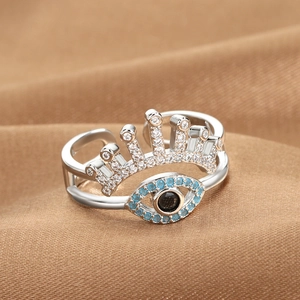 Silver crown evil eye open ring with blue and white zircons on warm fabric background